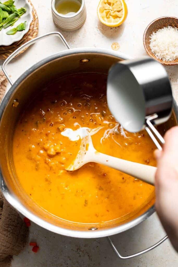 Heavy cream being poured into the soup in a pot
