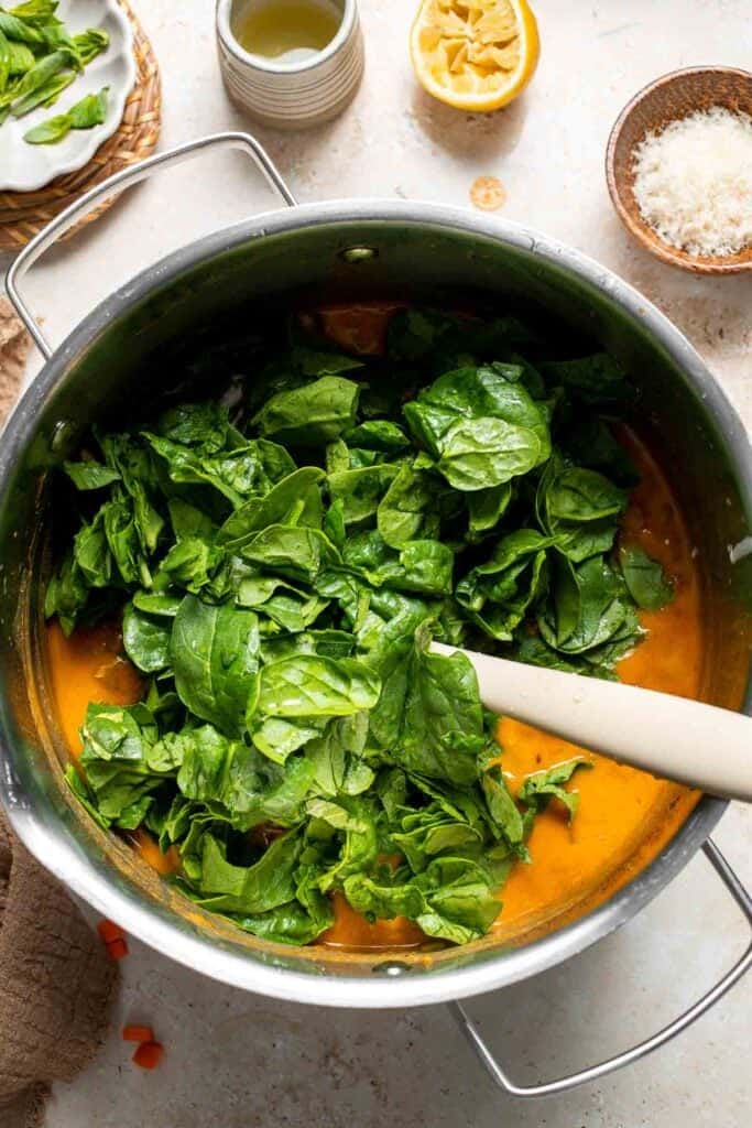 Fresh spinach being added to the soup in a pot