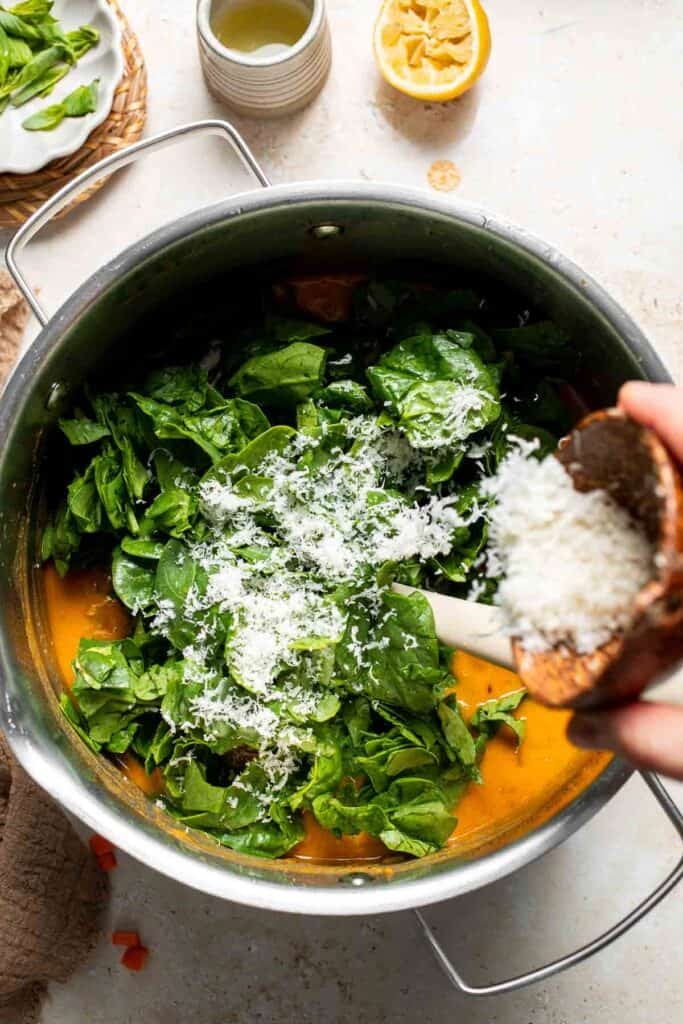 Parmesan cheese being sprinkled into the soup with spinach in a pot