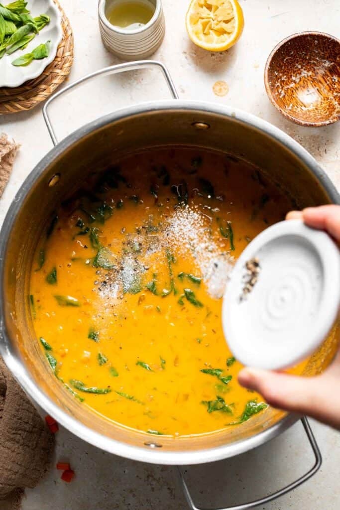 Salt and pepper being sprinkled into the finished soup in a pot