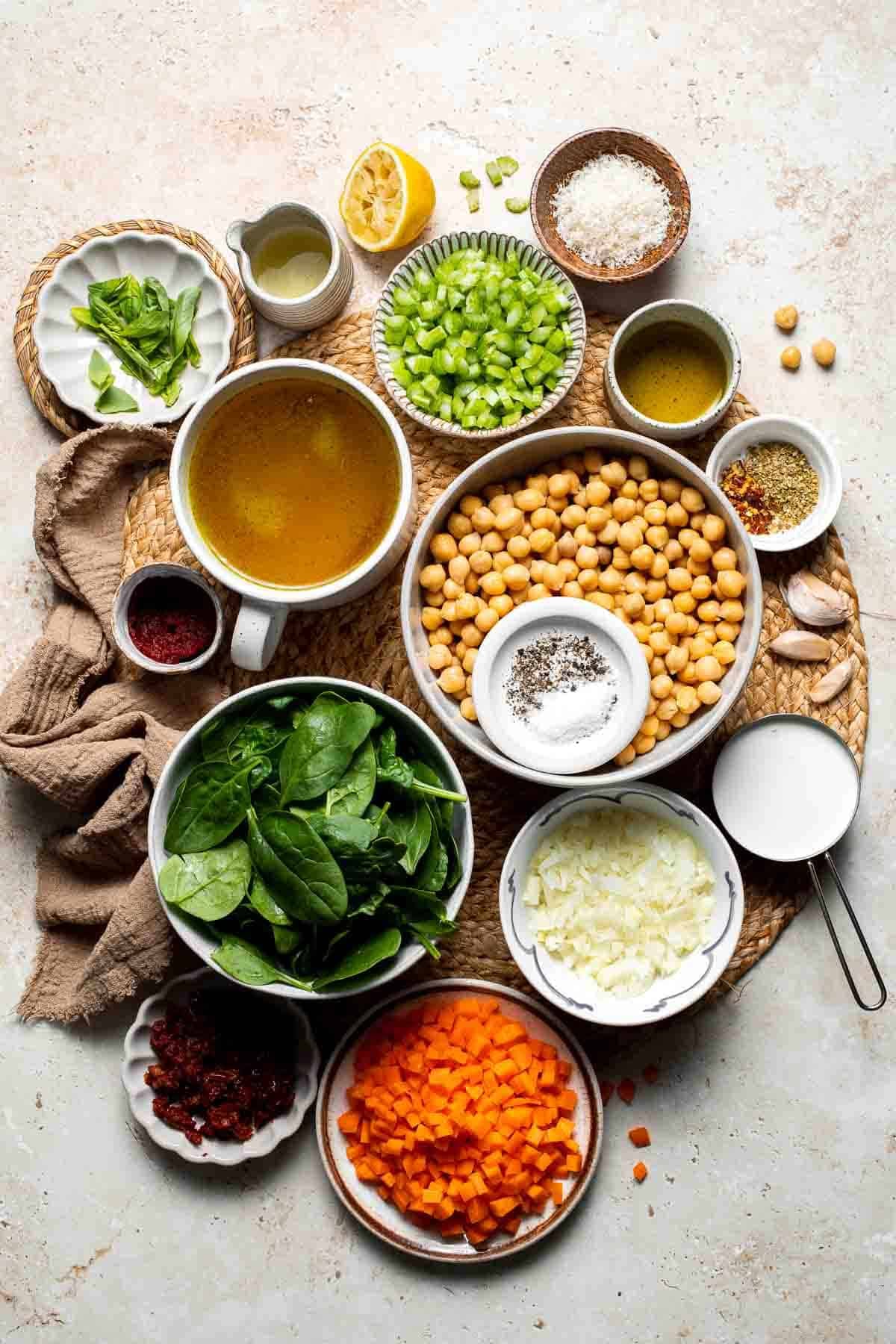 Ingredients for Tuscan chickpea soup including chickpeas, spinach, carrots, and sun-dried tomatoes arranged on a table