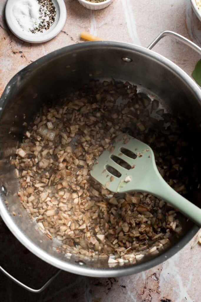 Mushrooms and onion cooking down with a spatula in a pot