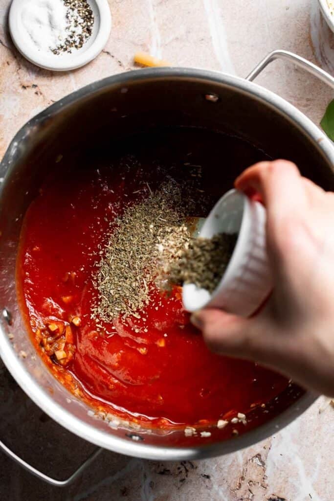 Italian seasoning being added to marinara sauce in a pot