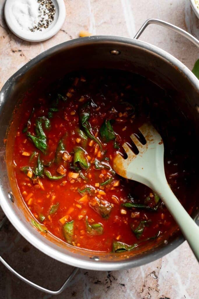 Spinach wilting into marinara sauce in a pot