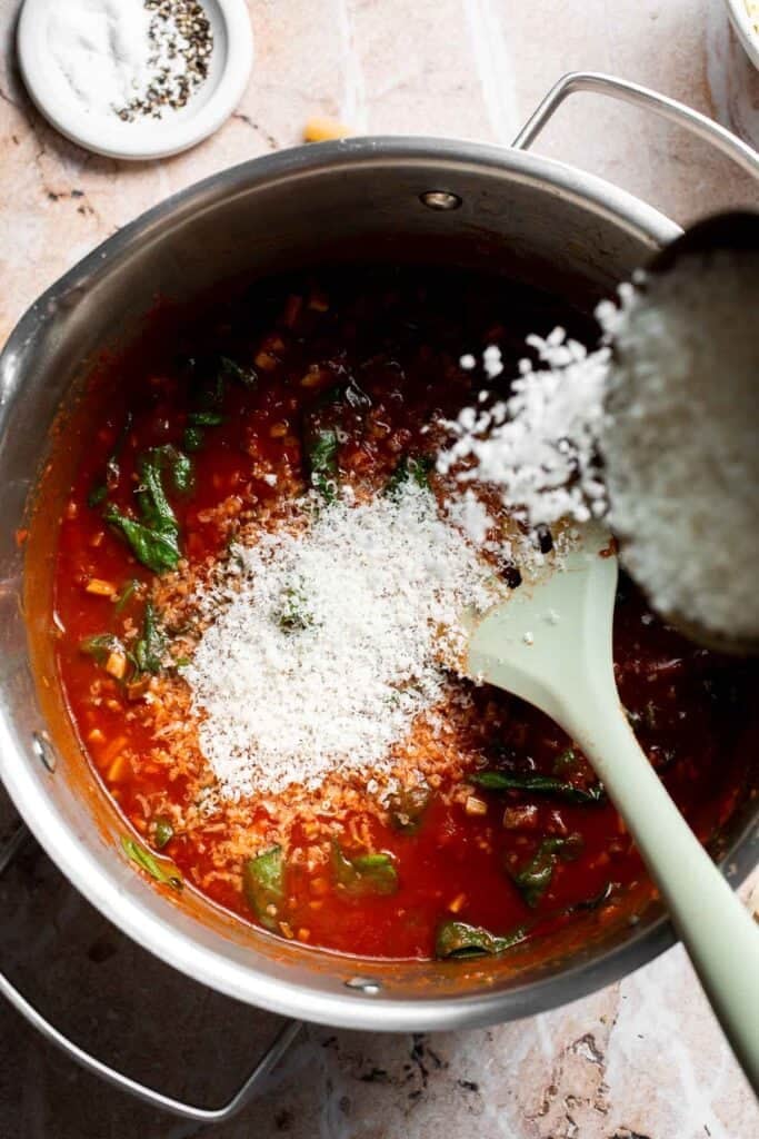 Parmesan cheese being sprinkled into marinara sauce in a pot