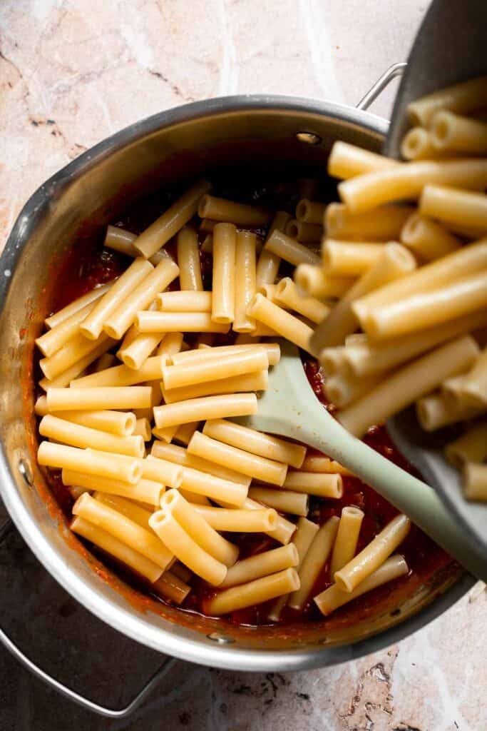 Cooked ziti pasta being added to marinara sauce mixture in a pot