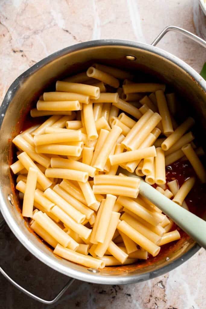Cooked pasta and marinara sauce being tossed together in a pot
