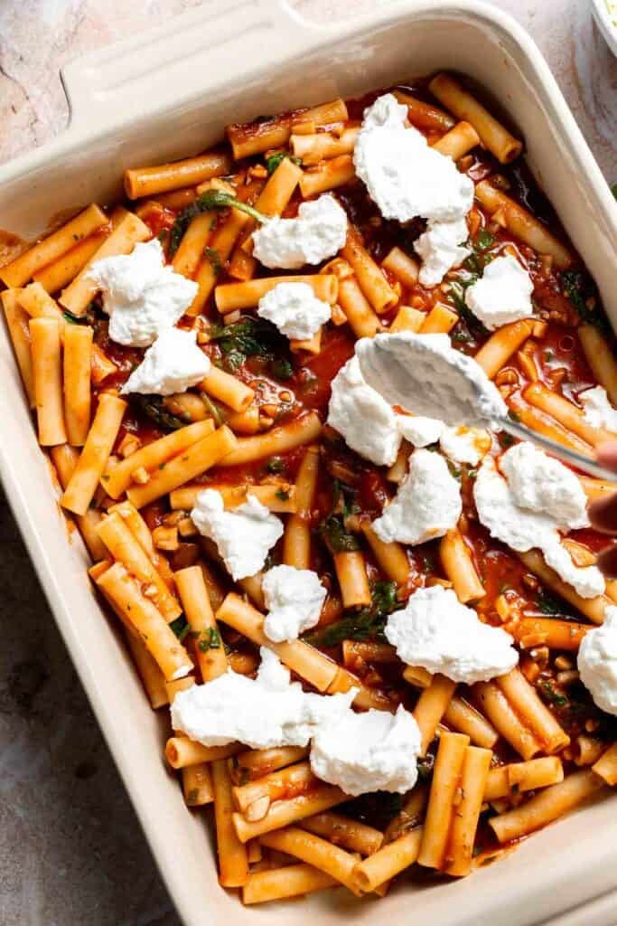 Dollops of ricotta mixture added over pasta in a baking dish