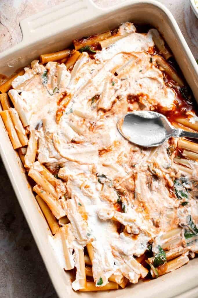 Ricotta mixture being spread over pasta in a baking dish