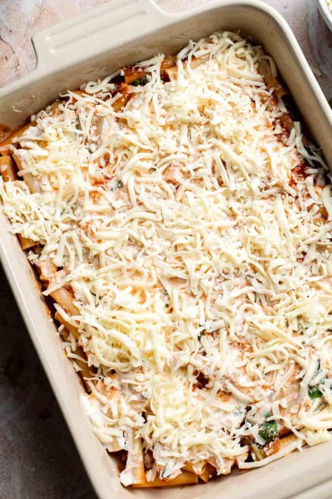 Shredded mozzarella cheese layered over pasta in a baking dish