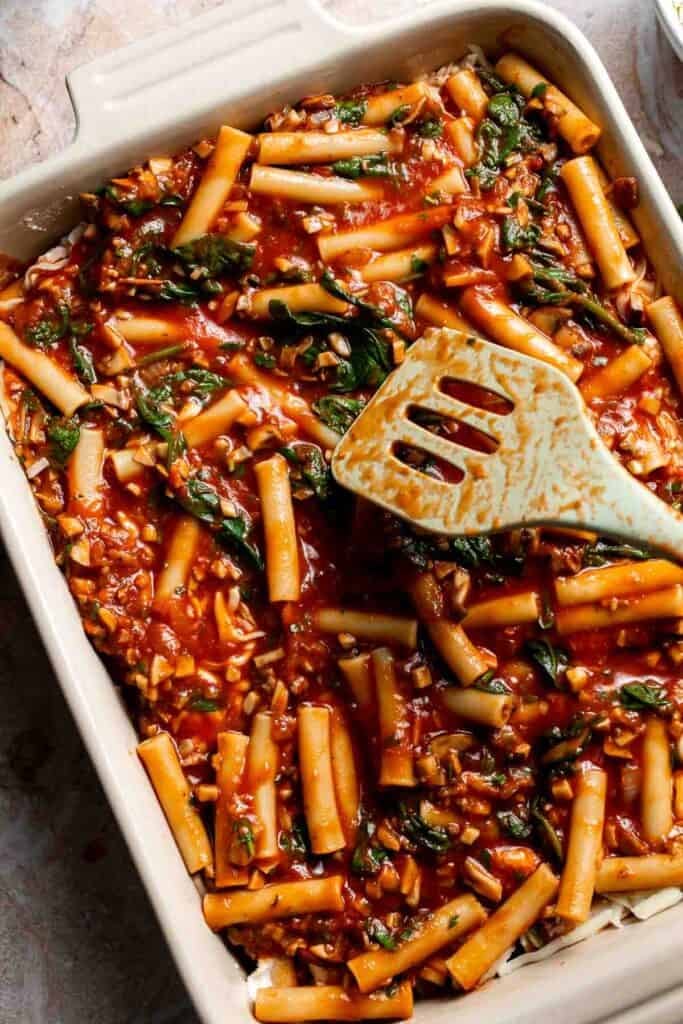 A second layer of pasta and sauce being added over cheese in a baking dish