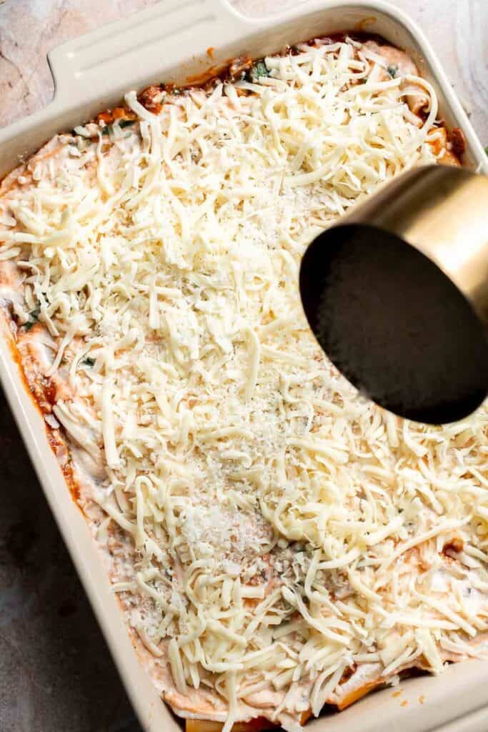 Parmesan cheese being sprinkled over the top of unbaked baked ziti