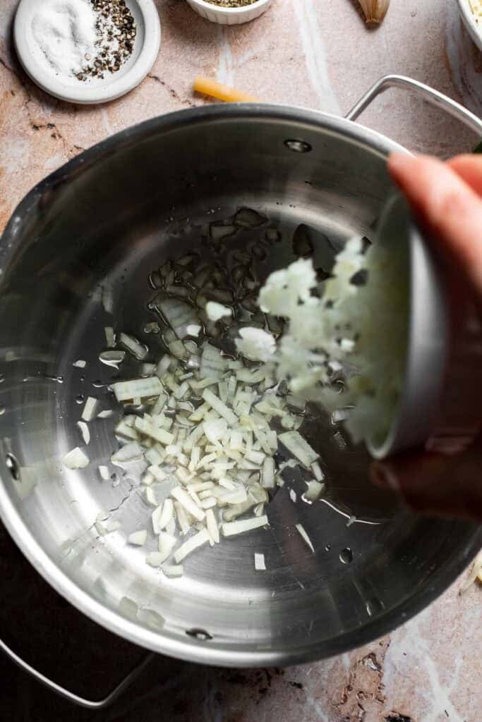 Diced onion being added to a pot with olive oil