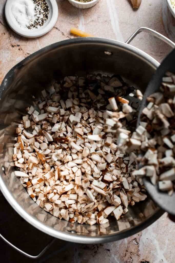 Finely chopped mushrooms being added to sautéed onion in a pot