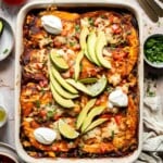 Overhead view of vegetarian enchilada casserole garnished with avocado, lime, and sour cream