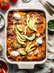 Overhead view of vegetarian enchilada casserole garnished with avocado, lime, and sour cream