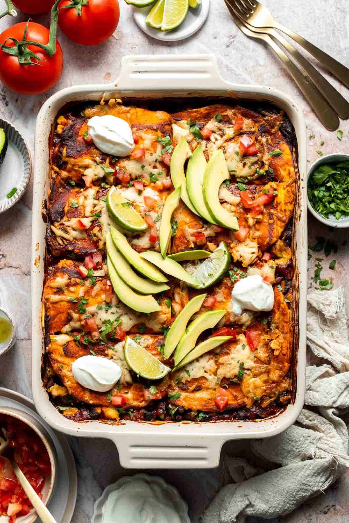 Overhead view of vegetarian enchilada casserole garnished with avocado, lime, and sour cream