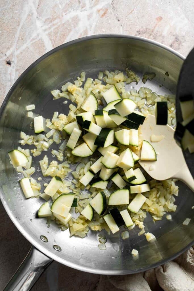 Diced zucchini added to sautéed onion and garlic in a skillet