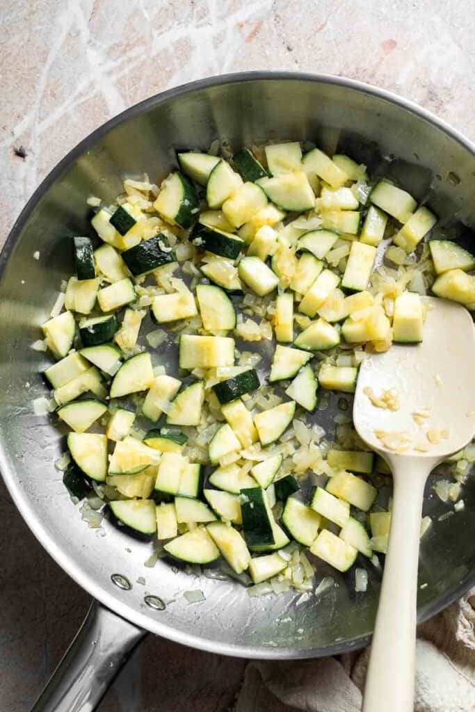 Diced zucchini cooking with onion and garlic in a skillet