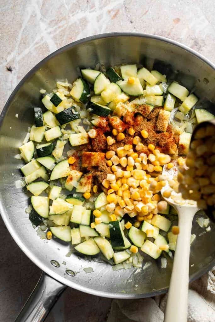 Corn being added into sautéed zucchini and onion in a skillet
