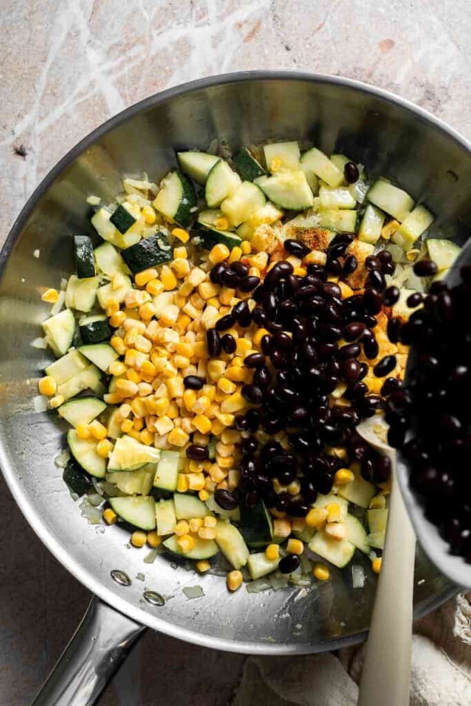 Black beans being added to a skillet of sautéed vegetables
