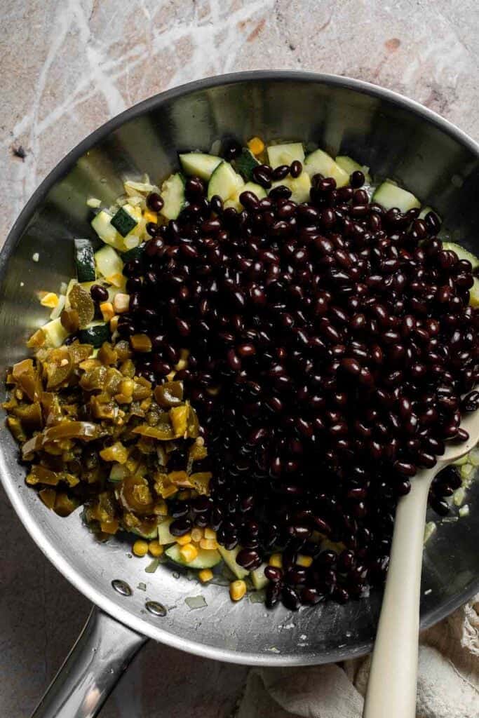 Black beans stirred into vegetable filling in a skillet