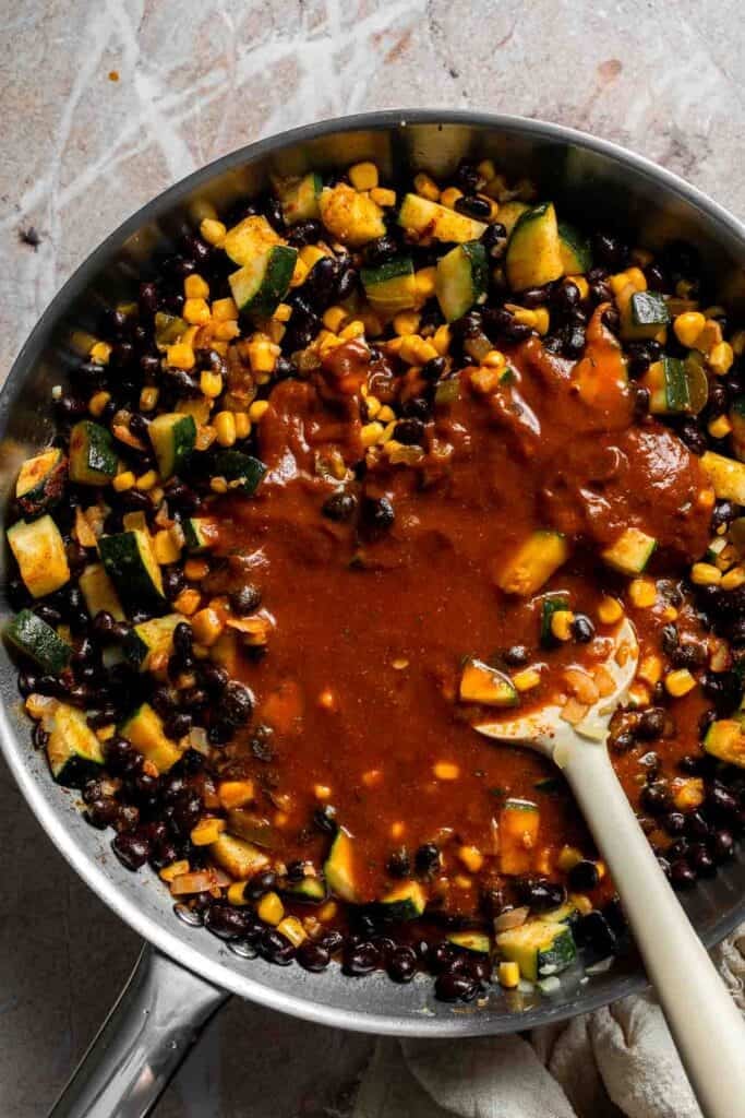 Enchilada sauce stirred into vegetable and black bean filling in a skillet