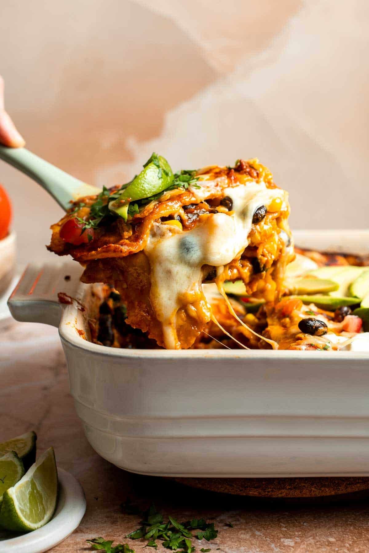 A slice of vegetarian enchilada casserole being lifted from the baking dish