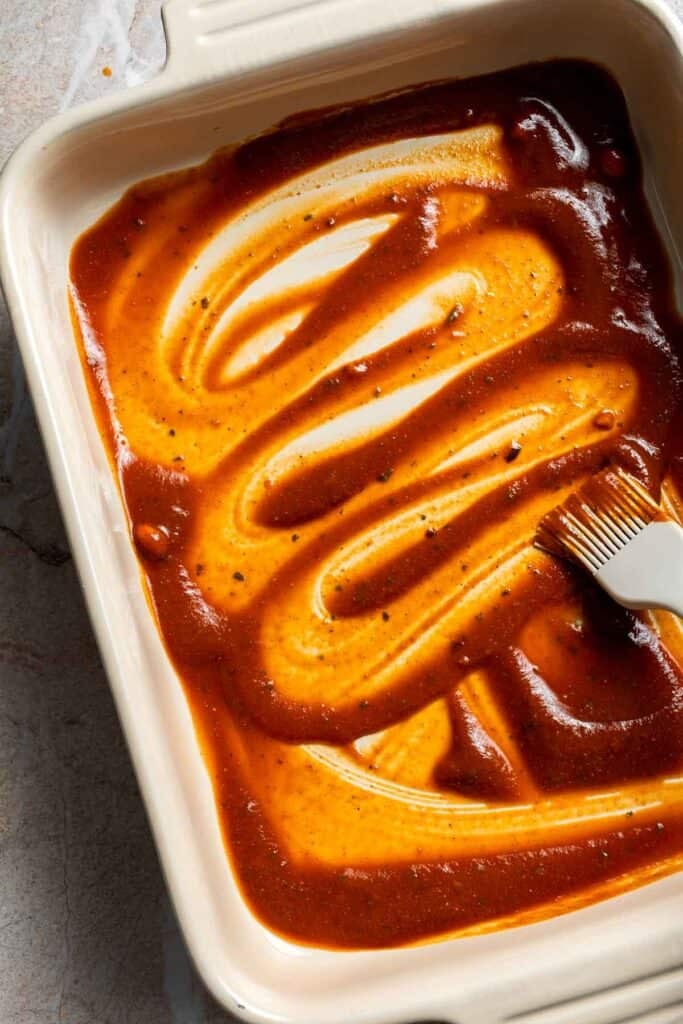Enchilada sauce spread across the bottom of a casserole dish