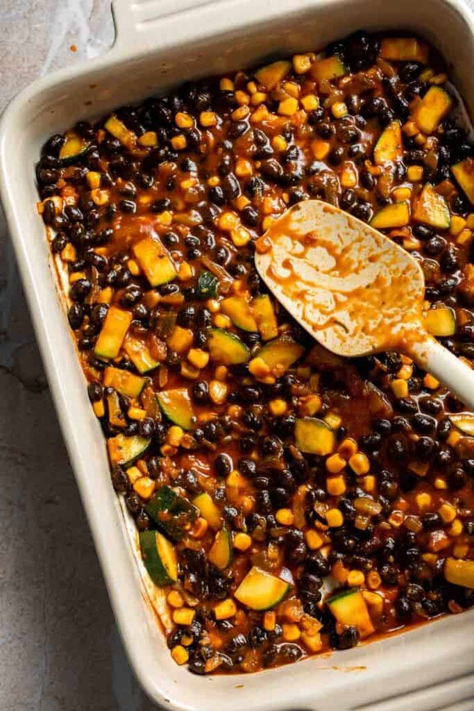 Vegetable and black bean filling spread over a layer of tortillas in a casserole dish