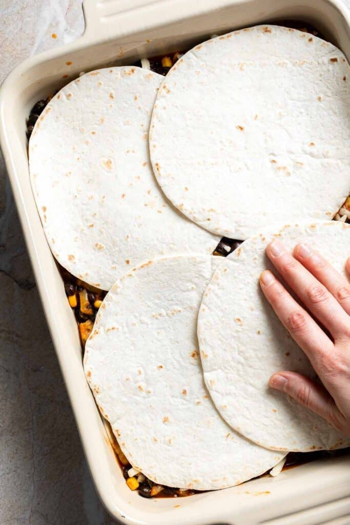 A second layer of tortillas being added to a casserole dish