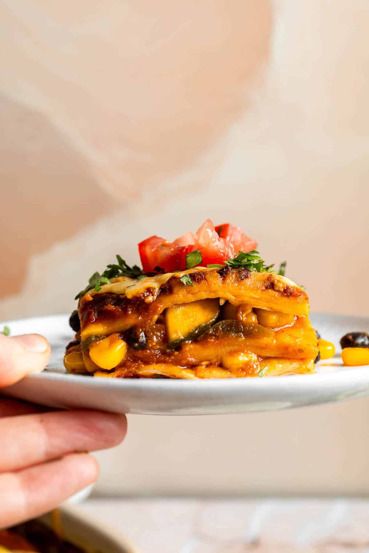 A plated serving of vegetarian enchilada casserole garnished with fresh herbs and tomatoes