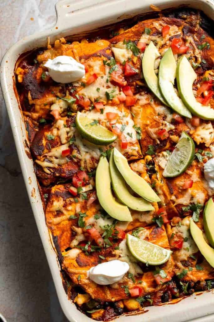 Vegetarian enchilada casserole topped with sliced avocado and sour cream