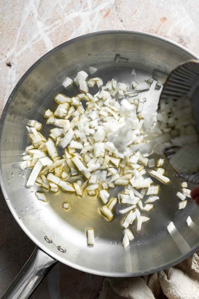 Diced onion being added to a skillet of oil