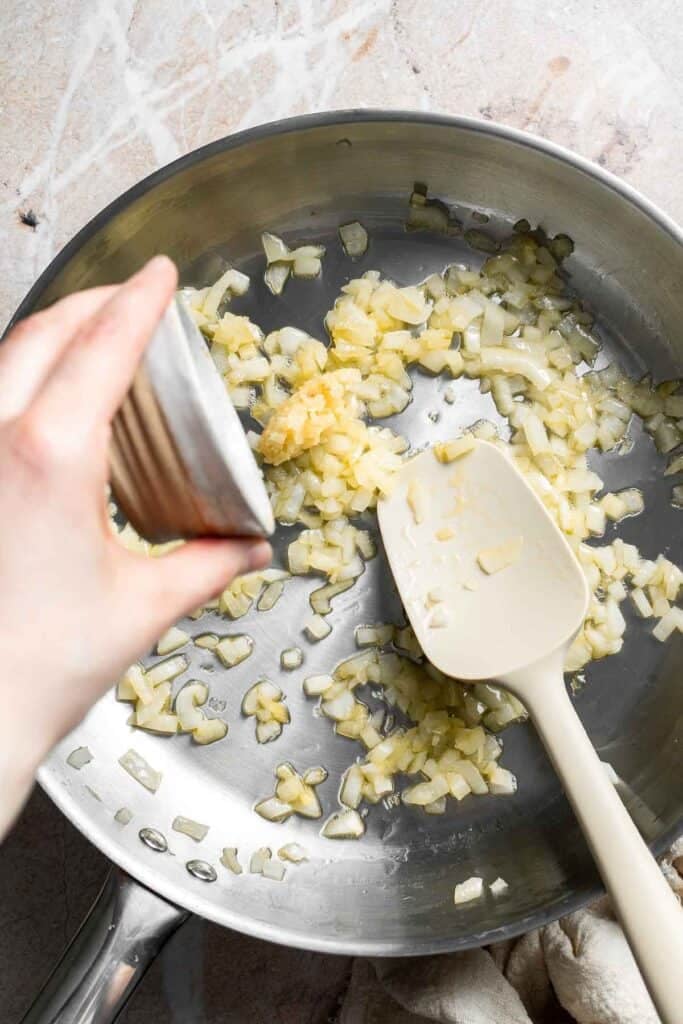 Minced garlic being added to sautéed onion in a skillet