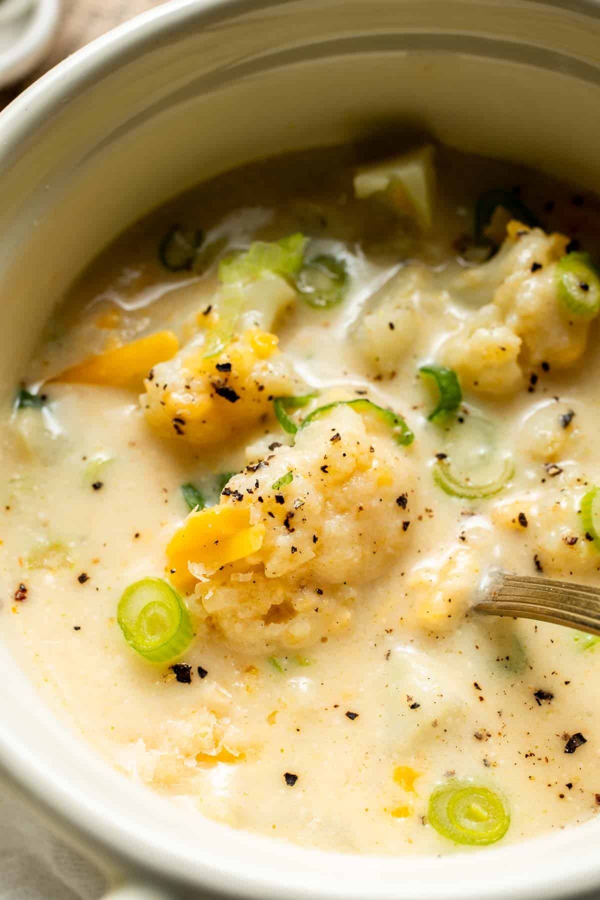 Close-up of cheesy cauliflower soup with tender cauliflower pieces, melted cheddar, and chopped green onions.