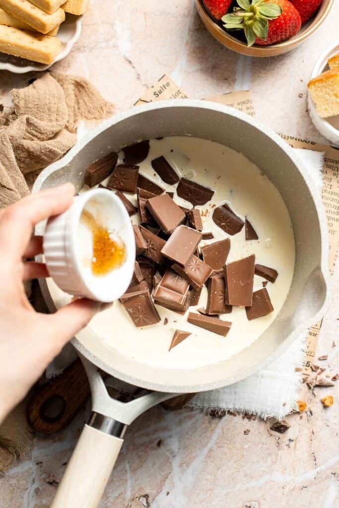 Adding vanilla extract to the chocolate and cream in the saucepan.