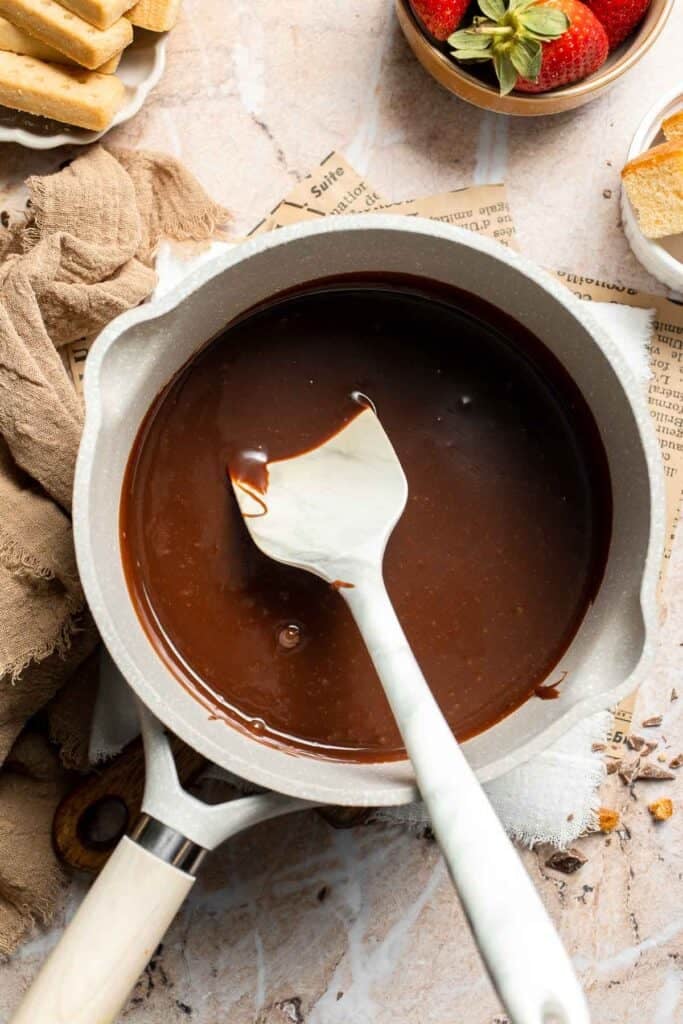 Smooth melted chocolate fondue in a saucepan with a spatula.