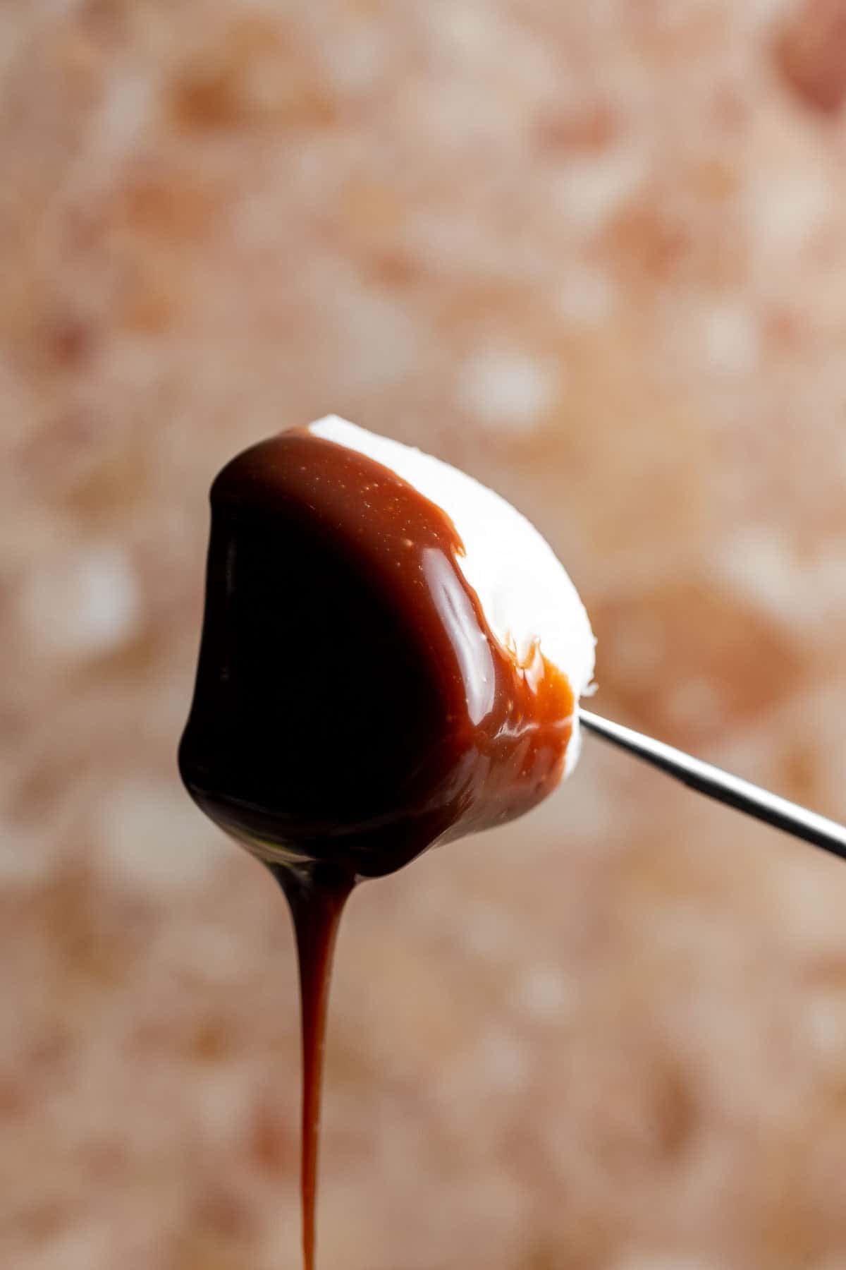 Marshmallow dipped in chocolate fondue on a fondue fork, with melted chocolate dripping from the bottom.