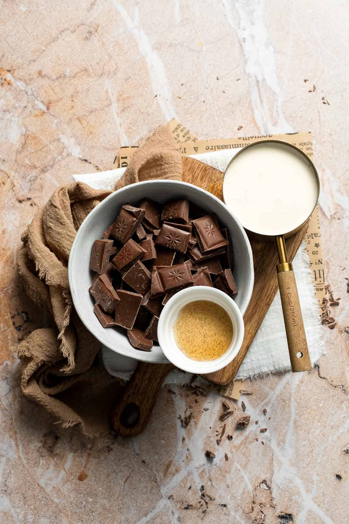 Ingredients for chocolate fondue, including chopped semisweet chocolate, heavy cream, and vanilla extract, on a marble surface.