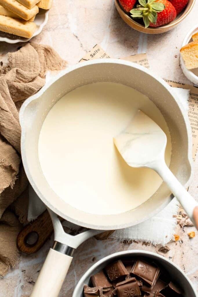 Heavy cream warming in a saucepan, stirred with a spatula.