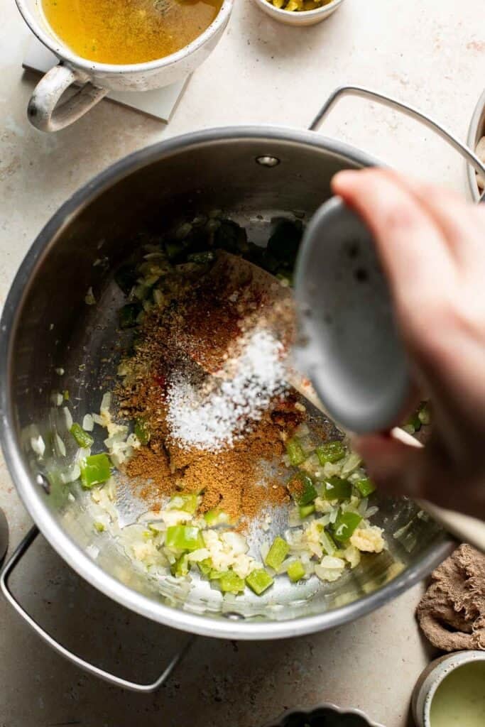 Sprinkling salt over the spices and vegetables in the pot.