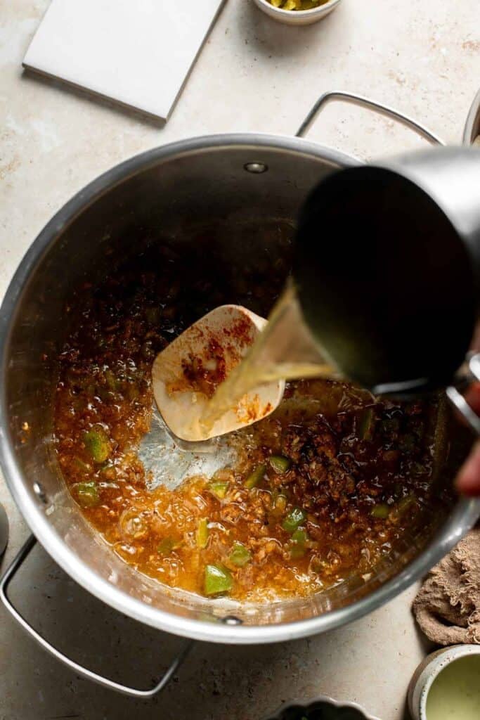 Pouring vegetable broth into the pot of toasted spices.