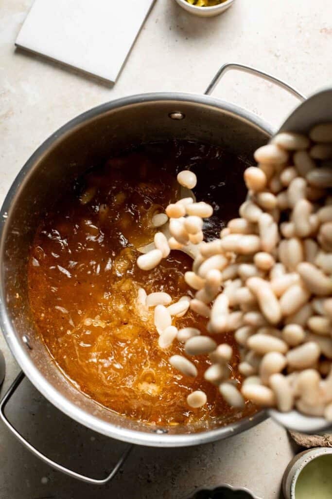 Adding cannellini beans to the broth in the pot.