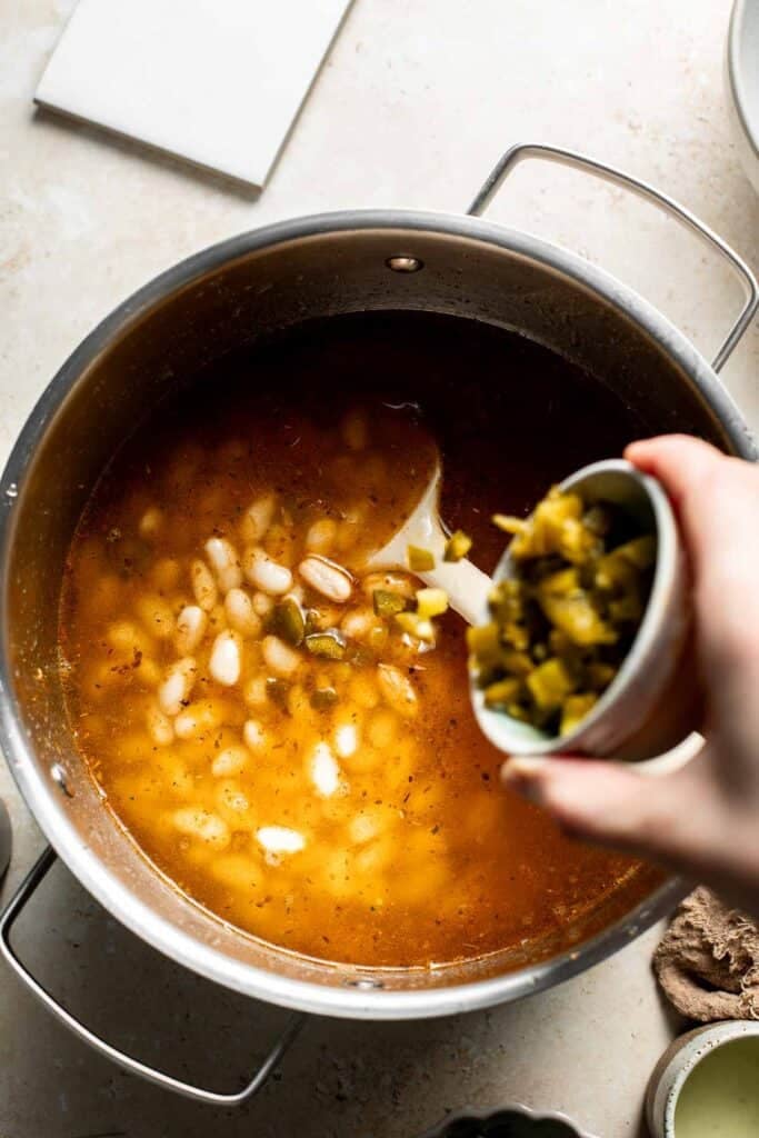Adding diced green chiles to the pot of broth and beans.