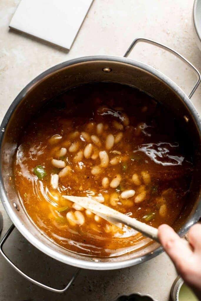 Stirring the beans and broth in the pot with a wooden spoon.