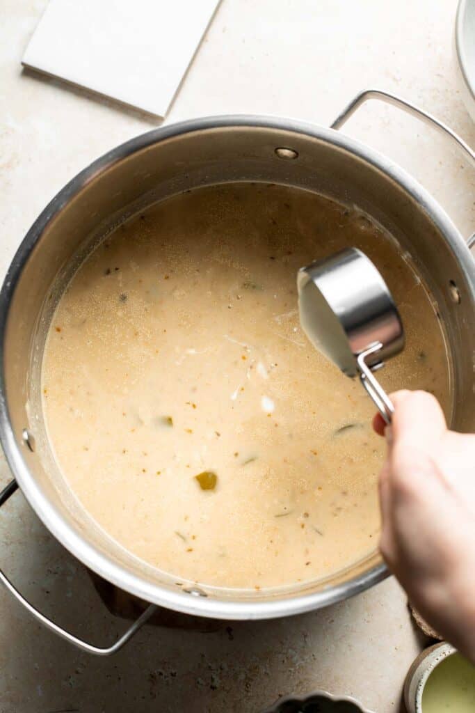 Adding sour cream to the creamy chili in the pot.