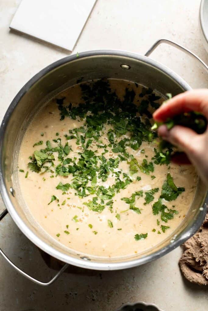 Sprinkling chopped fresh cilantro over the creamy chili in the pot.