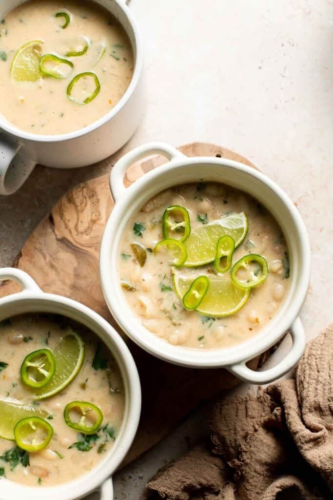 Bowls of creamy white bean chili topped with lime slices and sliced jalapeños.