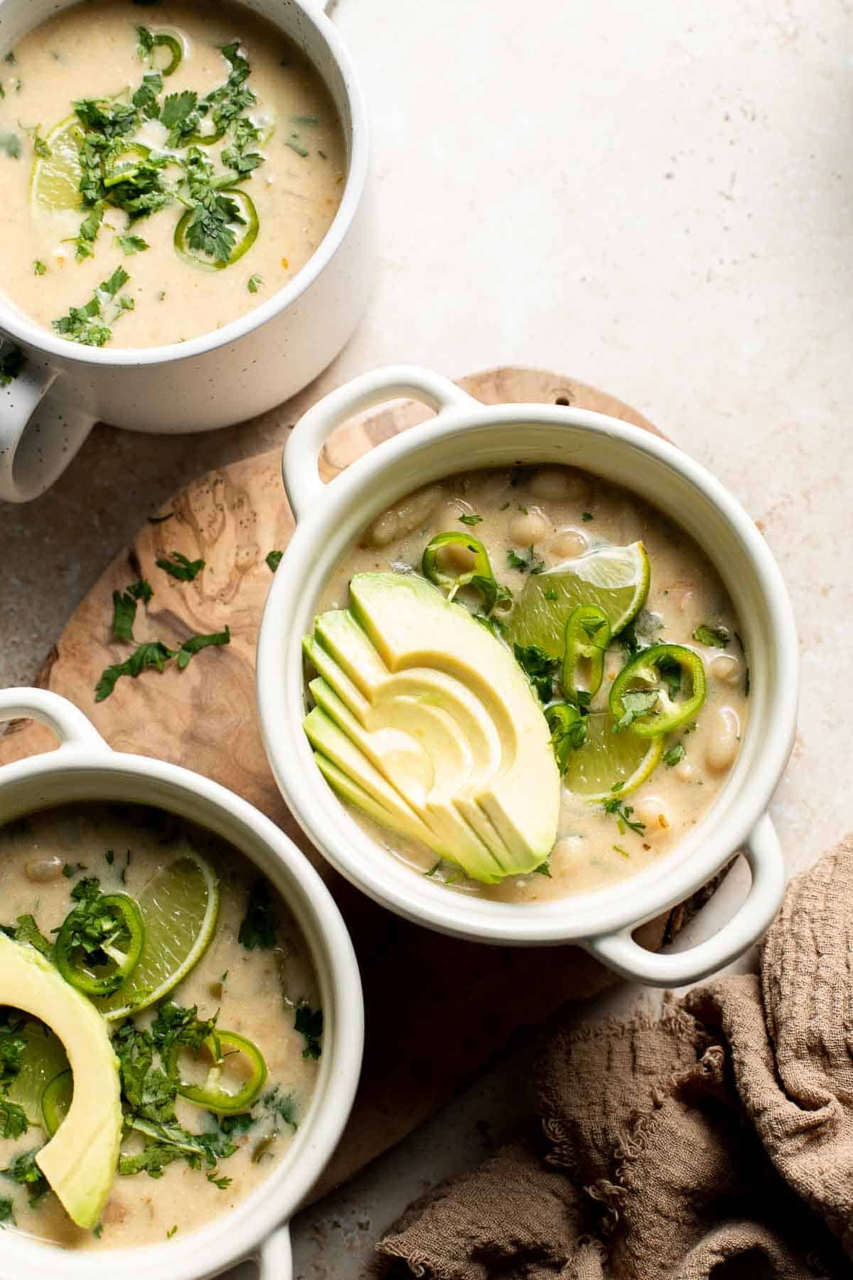 Bowls of creamy white bean chili topped with fanned avocado, cilantro, lime, and jalapeño.